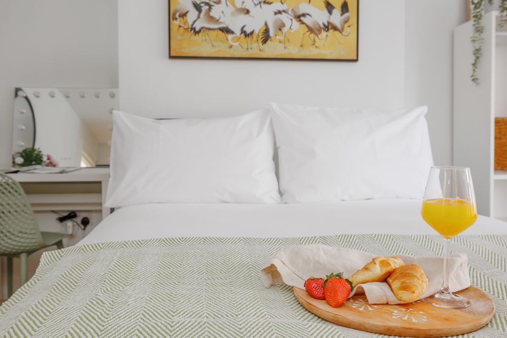 Close-up of a pillow on a bed with a board of croissants, strawberries, and a wine glass